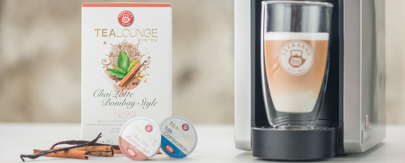 Tealounge Chai Latte Box, Zimtstangen, Teekapseln und Chai Latte unter einer Kaffeemaschine.