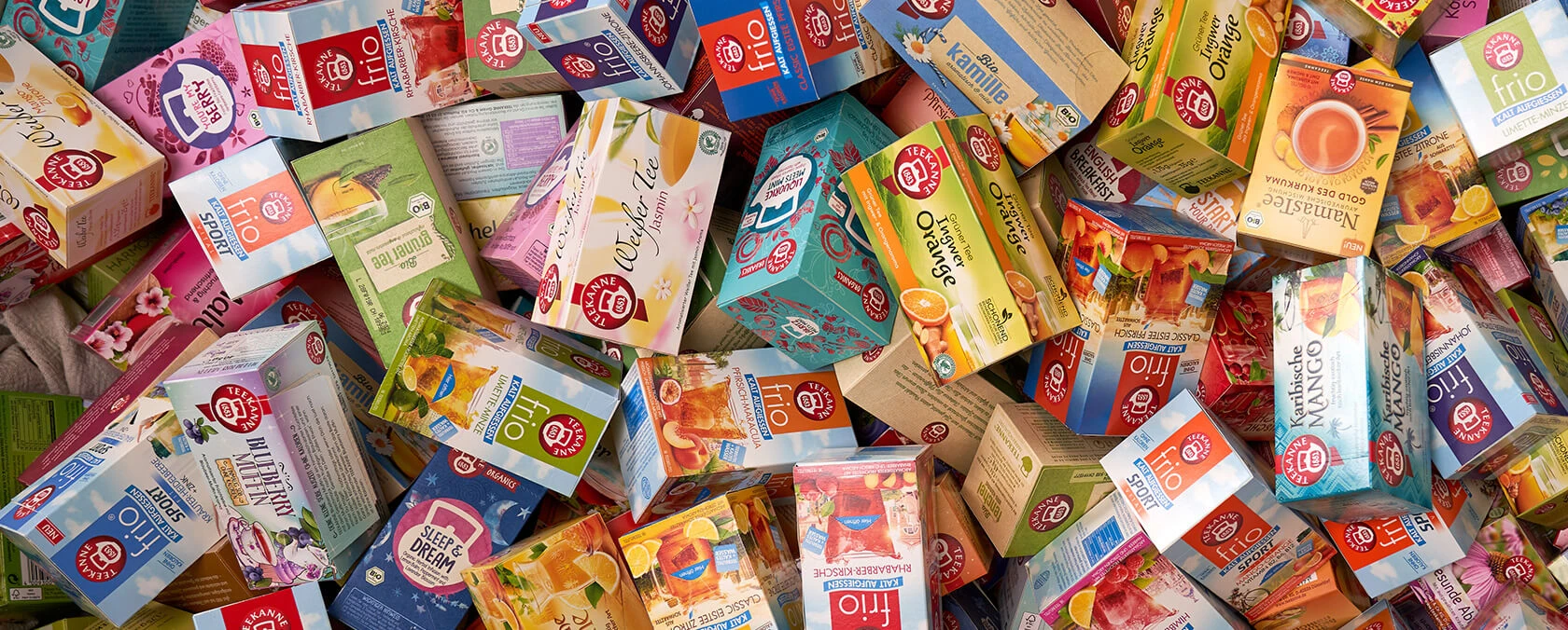 Verschiedene Teekanne-Teeboxen in bunten Verpackungen, gestapelt und verstreut in einem großen, unordentlichen Stapel.