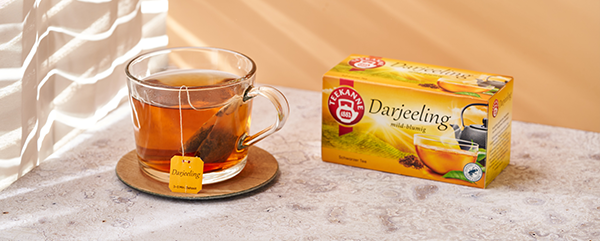 Glastasse mit Darjeeling-Tee und gelber Teekanne auf sonnenbeschienener Marmorfläche.