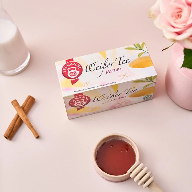 Teekanne Weisser Tee Jasmin-Box mit Milch, Zimtstangen, Honig und rosa Rose in der Nähe.