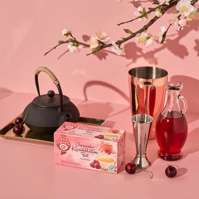 Japanisches Kirschblütenteeset mit Kirschen und Blütenzweig auf rosa Hintergrund.