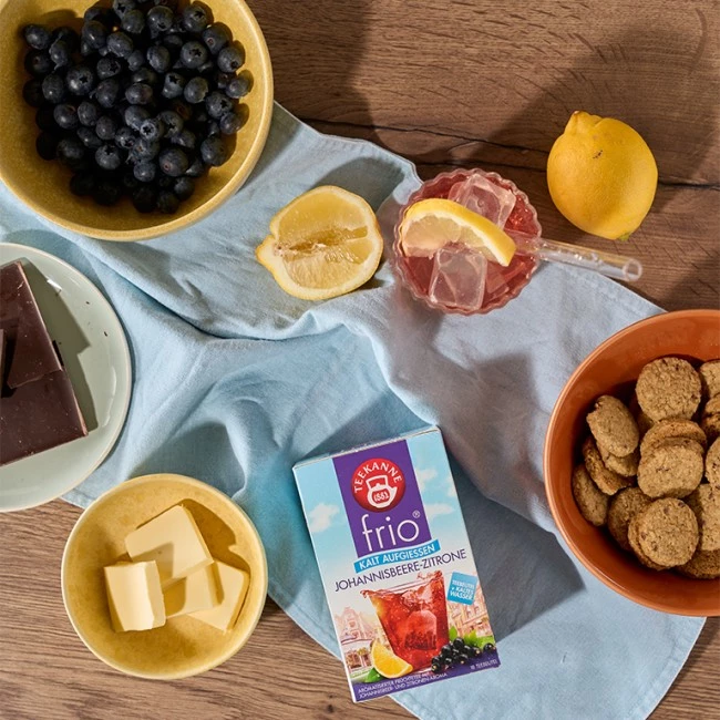 Flache Lage aus Blaubeeren, Zitrone, Schokolade, Butter, Keksen, rosa Getränk mit Zitrone und Frio-Tee.