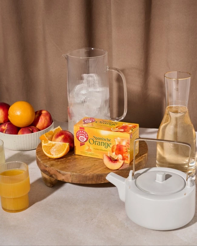 Frühstückstisch mit Orangen, Nektarinen, Orangensaft, Eiswasserkrug, Teekanne und spanischem Orangentee.