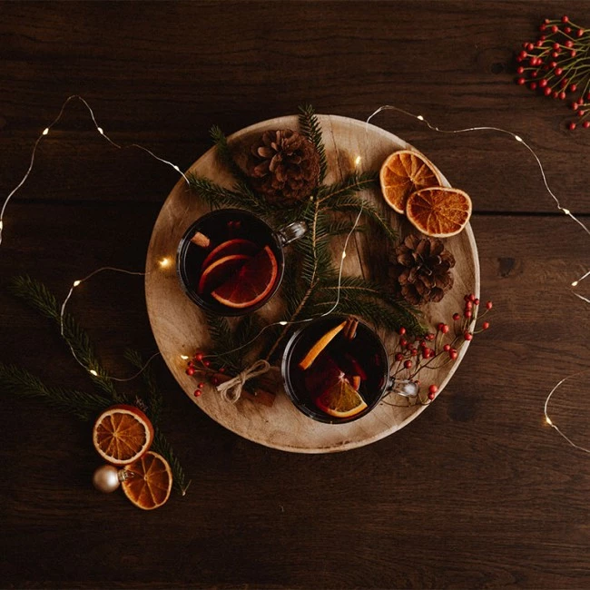 Zwei Tassen Glühwein mit Orangenscheiben und Zimt, umgeben von festlicher Winterdekoration.
