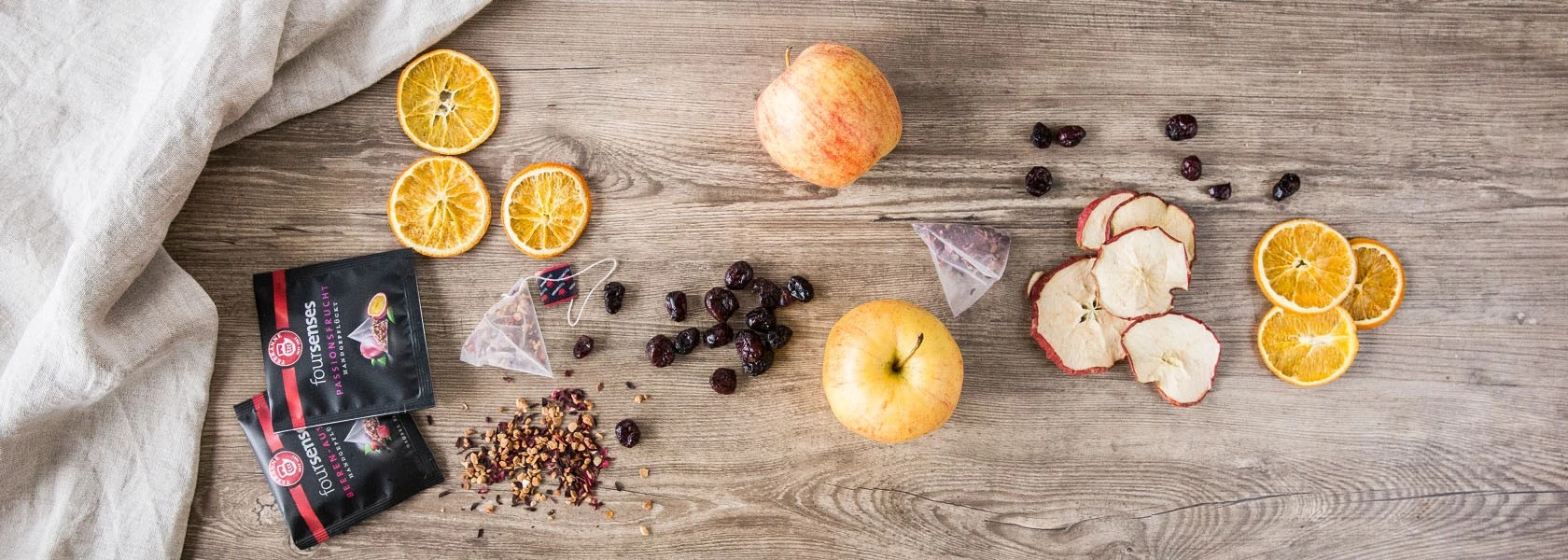 Trockenfrüchte, loser Tee, Teebeutel, Apfel und Beeren auf Holz mit leichtem Stoff.