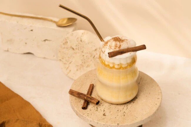 Eiskalte Latte mit Milchschaum, Zimt und Stäbchen im Glas auf dem Tablett, Metallstrohhalm, zusätzliche Stäbchen in der Nähe.