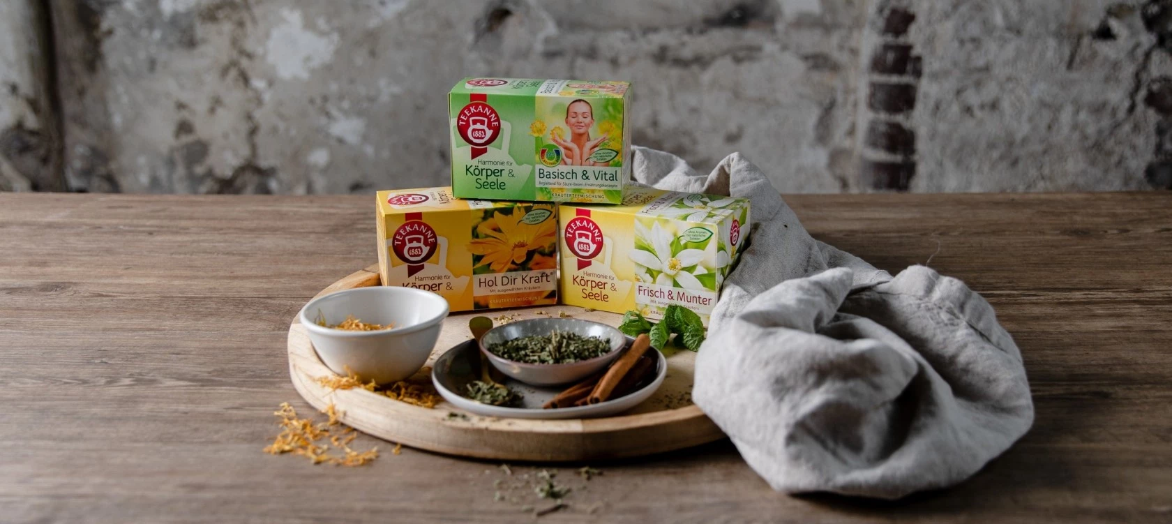 Kräuterteeboxen, getrocknete Kräuter, Zimtstangen und Blätter auf einem Tablett auf einem Holztisch.