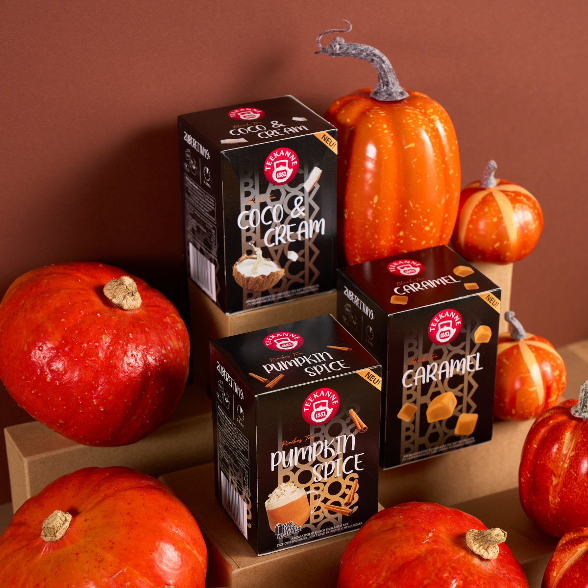 Eine Schachtel mit Kürbisgewürz-Getränkemischung ist zwischen dekorativen Kürbis auf braunen Plattformen mit braunem Hintergrund gestapelt.