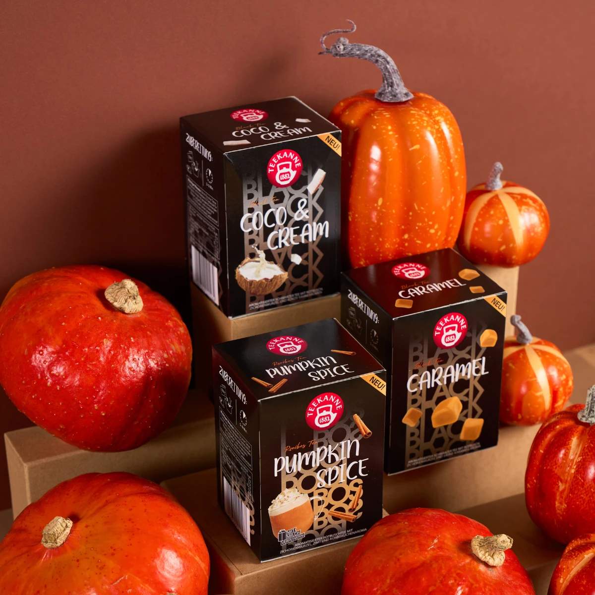 Eine Schachtel mit Kürbisgewürz-Getränkemischung ist zwischen dekorativen Kürbis auf braunen Plattformen mit braunem Hintergrund gestapelt.