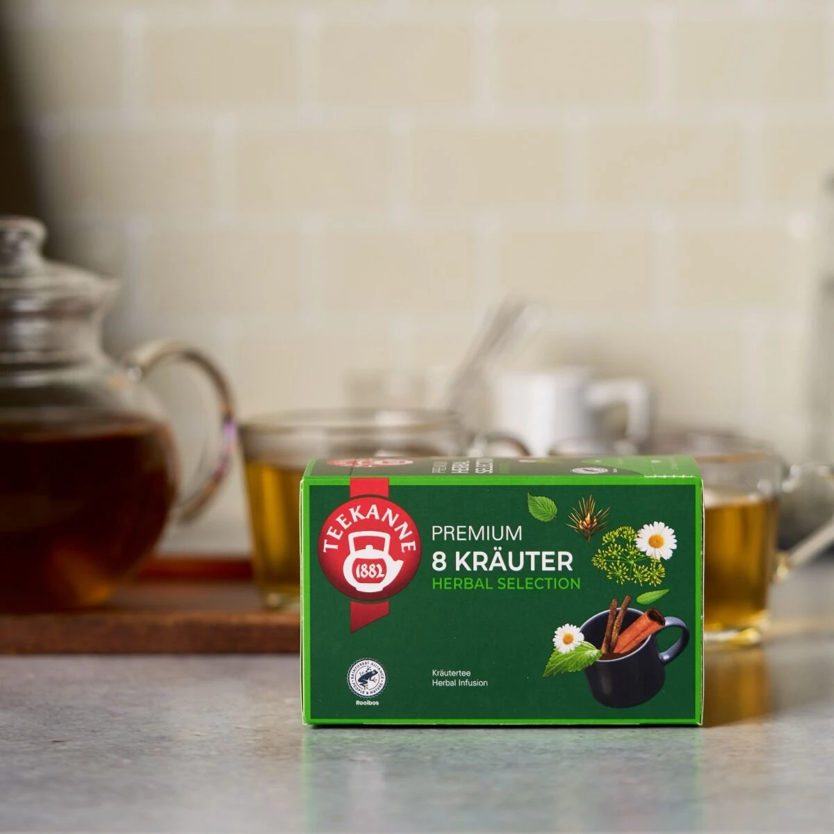 Eine Box Premium 8 Kräuter, unserer naturbelassenen Kräuterteemischung, steht auf der Theke. Genieße die frische Kräuterauswahl in Premium-Qualität - jetzt entdecken!.