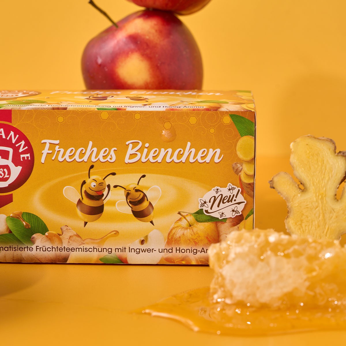 Eine Schachtel Verführerische Früchtetees Mix & Match-Tee auf gelbem Hintergrund mit Bienen, Waben, Ingwerwurzel, einem roten Apfel und Honig – perfekt zum Mix & Match oder als Angebot.