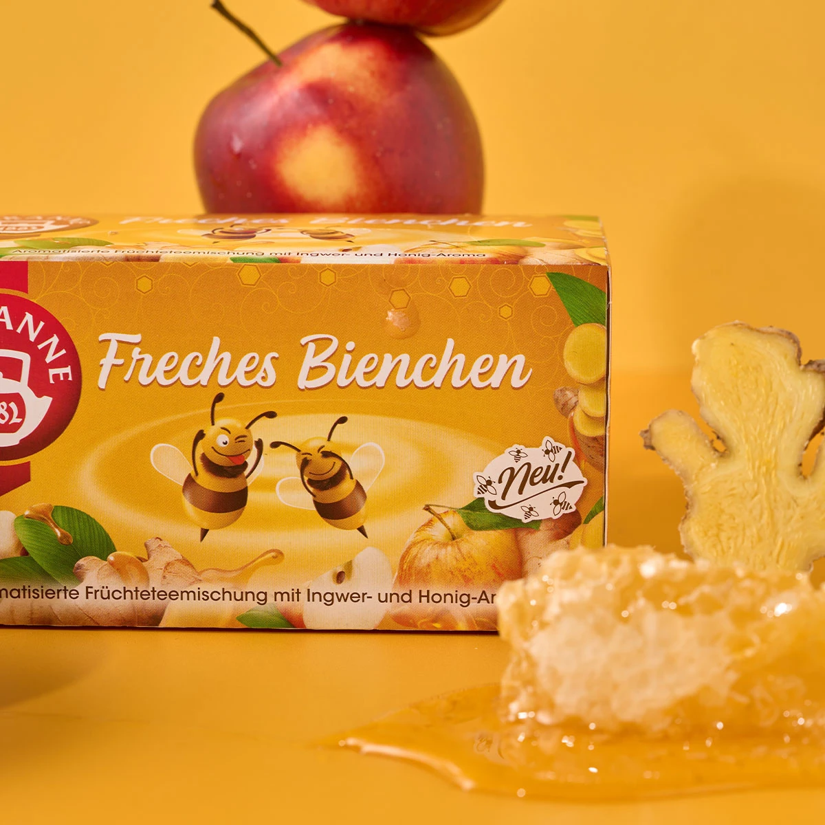 Eine Schachtel Verführerische Früchtetees Mix & Match-Tee auf gelbem Hintergrund mit Bienen, Waben, Ingwerwurzel, einem roten Apfel und Honig – perfekt zum Mix & Match oder als Angebot.