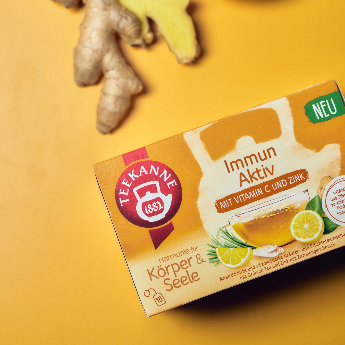 Eine Schachtel Immun Aktiv-Tee mit Vitamin C und Zink steht neben frischem Ingwer auf einer gelben Fläche. Auf der Verpackung sind eine Zitronenscheibe und Tee abgebildet, um die immununterstützenden Inhaltsstoffe hervorzuheben.