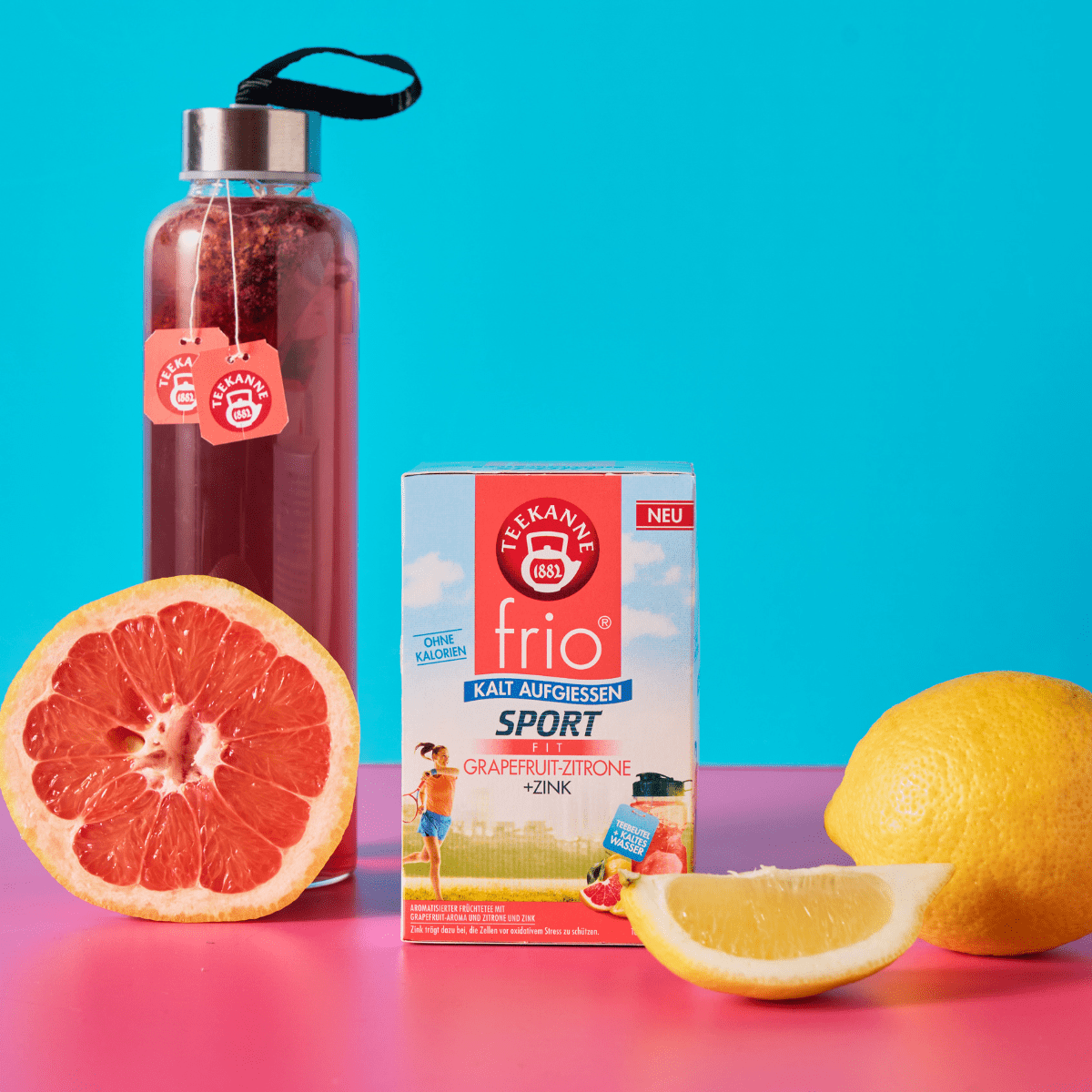 Eine Packung "frio Sport Fit Grapefruit-Zitrone", ein Tee zum kalt Aufgießen. Dazu eine Sport-Glasflasche mit aufgegossenem Tee. Dekoriert mit Grapefruit und Zitrone.