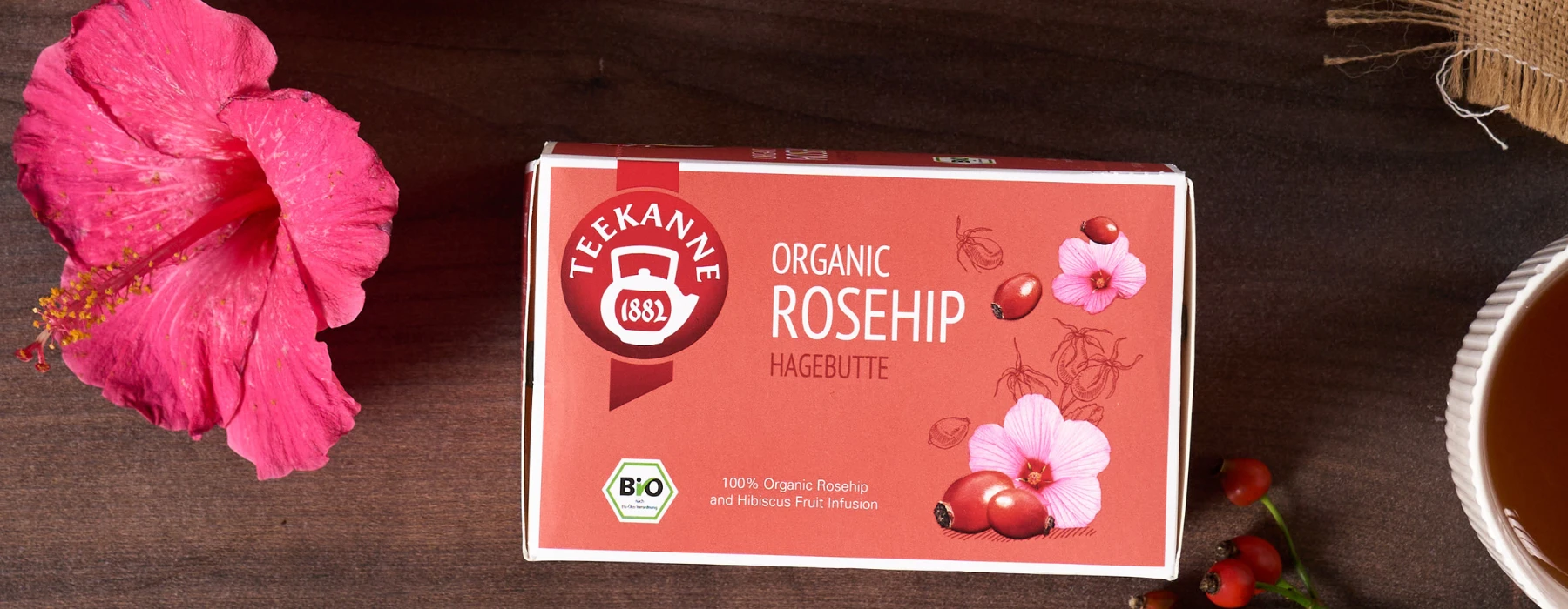 Eine Kiste Kuschelabend-Tee steht auf einem Holztisch mit zwei Birnen - eine ganz, eine halbiert -, während eine kuschelige Decke und warme Lichterdekoration eine gemütliche Kulisse schaffen.