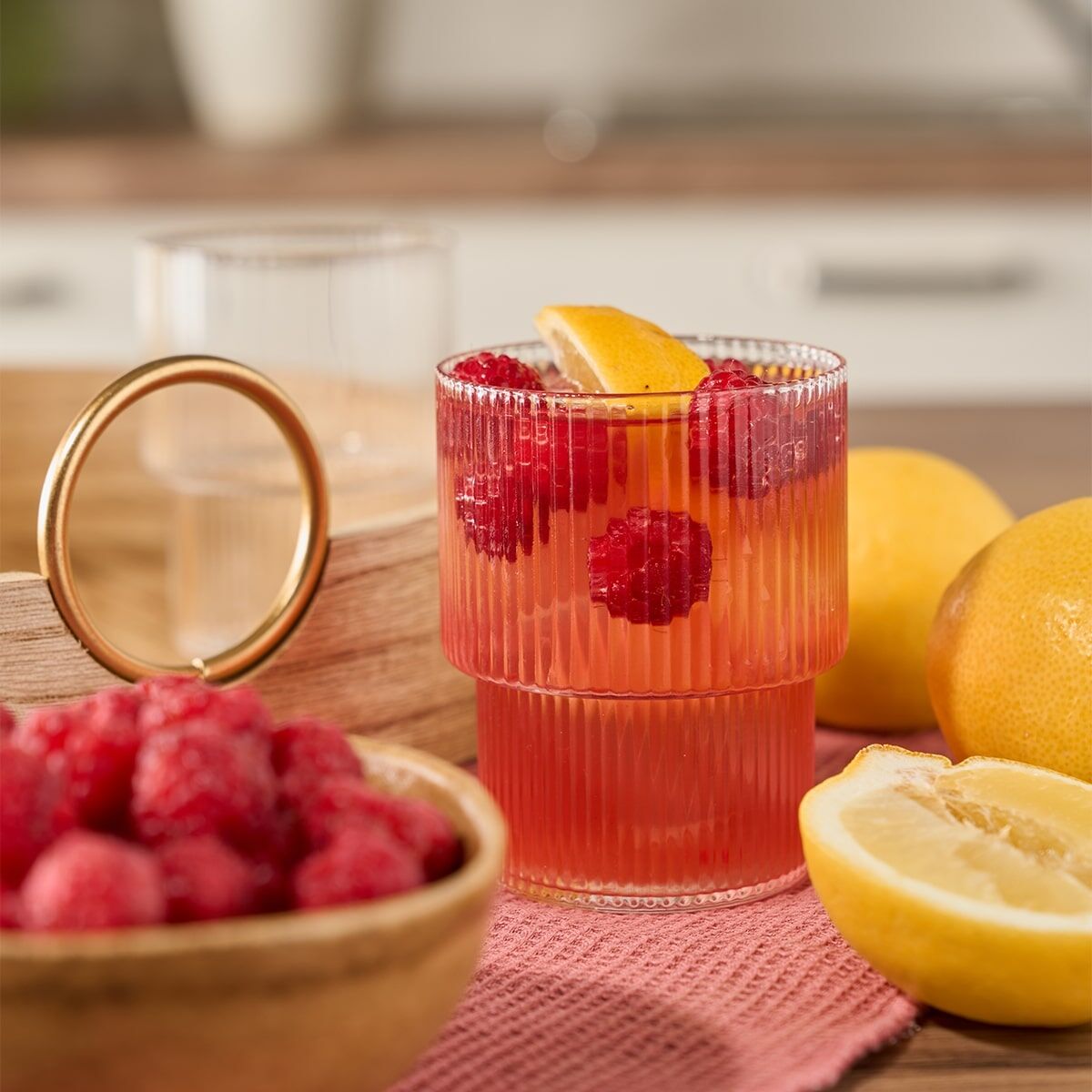 frio Tee in Glas mit Früchten auf einem Holztisch, Himbeeren und Zitronen rechts und links